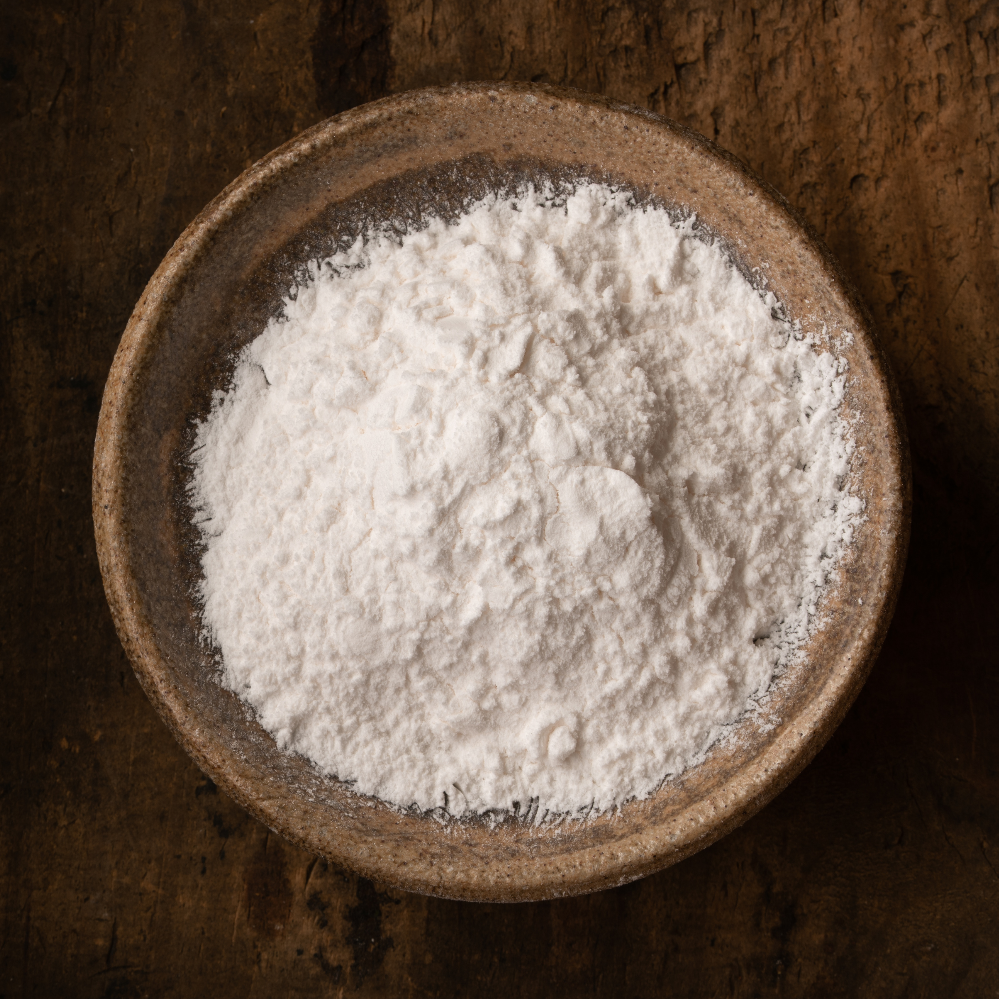 White powder in a brown bowl on a dark wooden surface