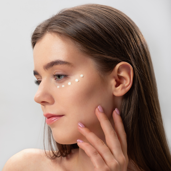 Woman applying a skincare product on her face with a neutral background