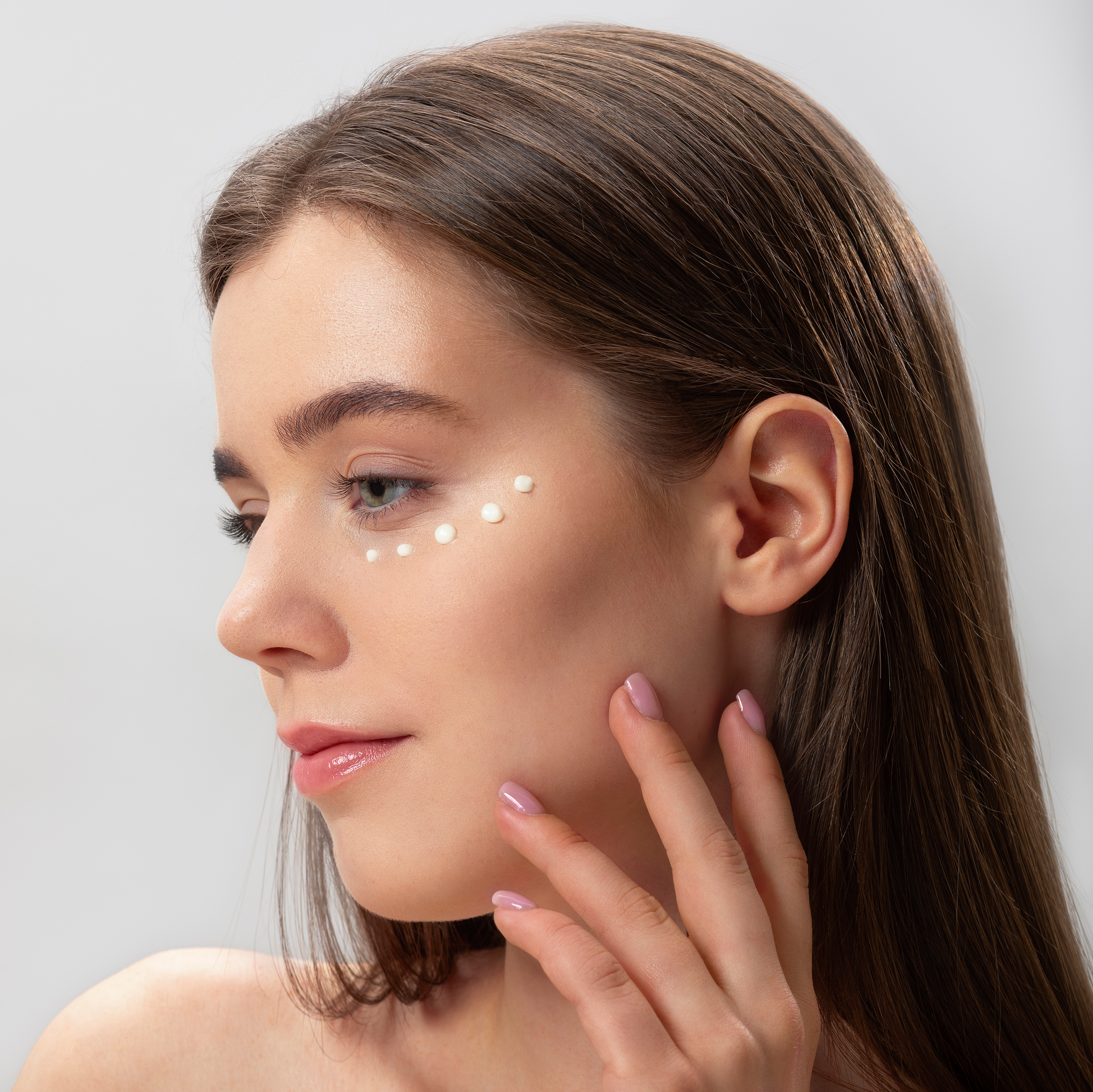 Woman applying a skincare product on her face with a neutral background